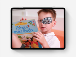 Photograph of child with eye patch reading on iPad Pro